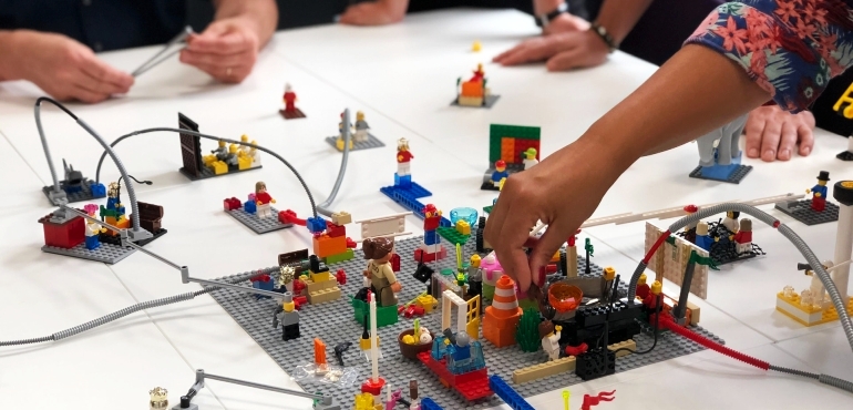 Hände bewegen mehrere miteinander verbundene Lego-Szenarien und verknüpfen diese untereinander
