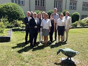 Auf dem Foto stehen neun Personen in einem Garten mit Rasen, Hecken und einem historischen Gebäude im Hintergrund. Die Gruppe hat sich für ein gemeinsames Bild aufgestellt und blickt lächelnd in die Kamera. Es sind Männer und Frauen unterschiedlichen Alters zu sehen, in teils formeller Kleidung. Anlass des Treffens ist die konstituierende Sitzung des neuen Tierschutzbeirats Mecklenburg-Vorpommern.