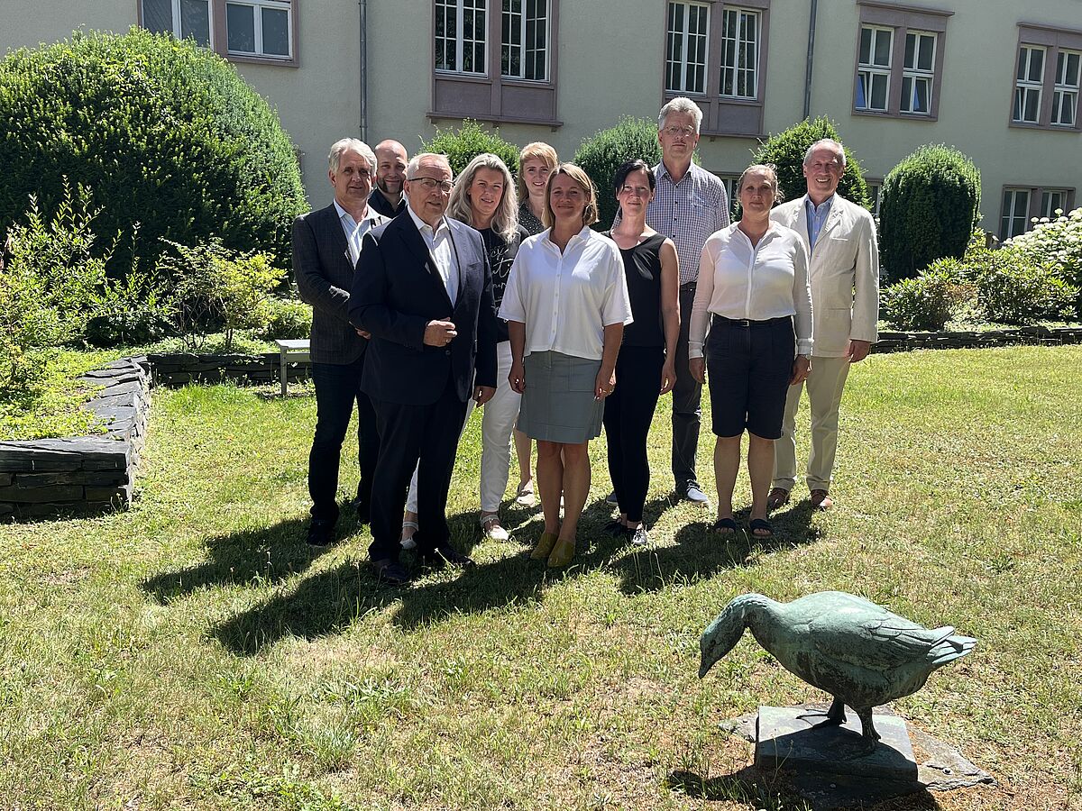 Auf dem Foto stehen neun Personen in einem Garten mit Rasen, Hecken und einem historischen Gebäude im Hintergrund. Die Gruppe hat sich für ein gemeinsames Bild aufgestellt und blickt lächelnd in die Kamera. Es sind Männer und Frauen unterschiedlichen Alters zu sehen, in teils formeller Kleidung. Anlass des Treffens ist die konstituierende Sitzung des neuen Tierschutzbeirats Mecklenburg-Vorpommern.