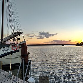 Der Blick vom Steg. Das Segelschiff Engelina liegt im Hafen und ist im Anschnitt des Fotos zu erkennen. Im Hintergrund ist der Himmel leicht eingefärbt. Wahrscheinlich geht die Sonne gerade auf oder unter.