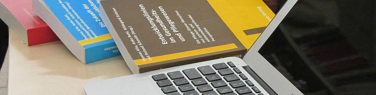 Bücher liegen neben einem MacBook auf dem Tisch