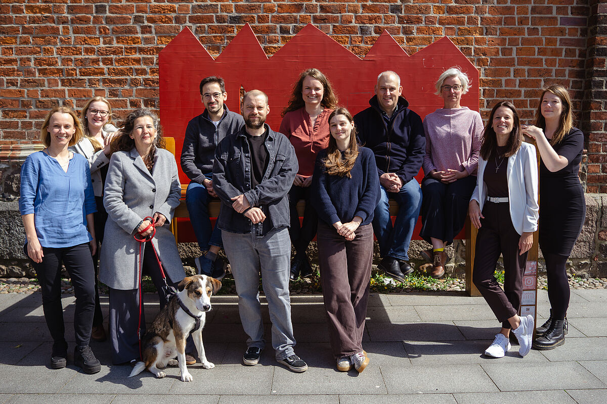 Das Foto zeigt das 11-köpfige Projektteam ARCHIPEL auf der Hochschulbank sitzend bzw. stehend vor der Konzertkirche in Neubrandenburg.