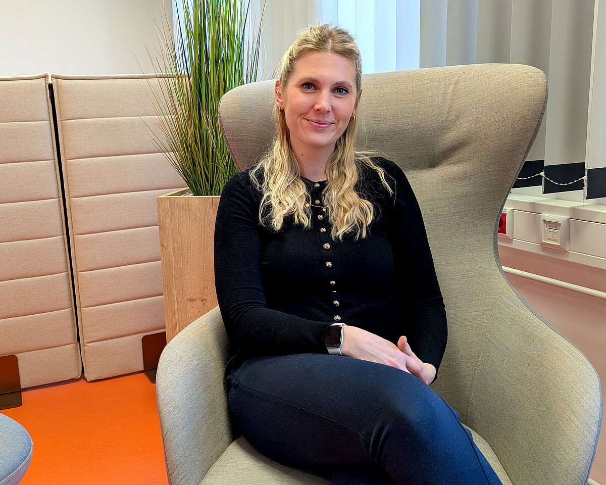 Eine Frau mit langen blonden Haaren und schwarzem Oberteil sitzt auf einem hellgrauen Sessel und lächelt freundlich in die Kamera. Die Studentin Anja Winkler erzählt im Interview von ihrem Weg ins Studium an der Hochschule Neubrandenburg.