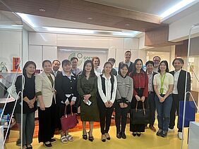 Eine Gruppe von Personen steht in zwei Reihen für ein Gruppenfoto bereit. Ihre Kleidung ist formlos und bunt. Im Hintergrund ist das Logo des Goethe-Instituts zu erkennen.