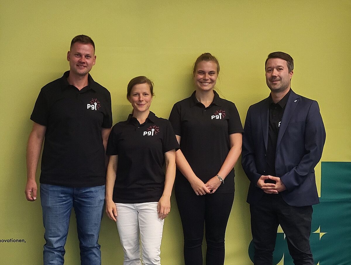Vier Personen lächeln freundlich in die Kamera. Sie tragen formidentische schwarze Poloshirts mit der Aufschrift pgi.