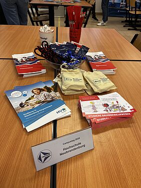 Zu sehen ist ein Tisch, gefüllt mit Werbeartikeln der Hochschule Neubrandenburg und des Studienkonzepts BLU. Im Vordergrund liegen Postkarten des Studiengangs Bauingenieurwesen und Flyer mit der Aufschrift "Studieren in Mecklenburg-Vorpommern".