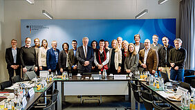 Zu sehen sind die Mitglieder des Wissenschaftlichen Beirats auf einem Gruppenfoto in einem Seminarraum. Die Personen stehen vor einer blauen, beleuchteten Wand mit der Aufschrift „Bundesministerium für Landwirtschaft, Ernährung und Heimat“.