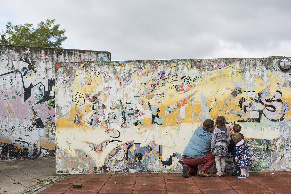 Mann mit zwei Kindern vor einer Graffiti-Wand